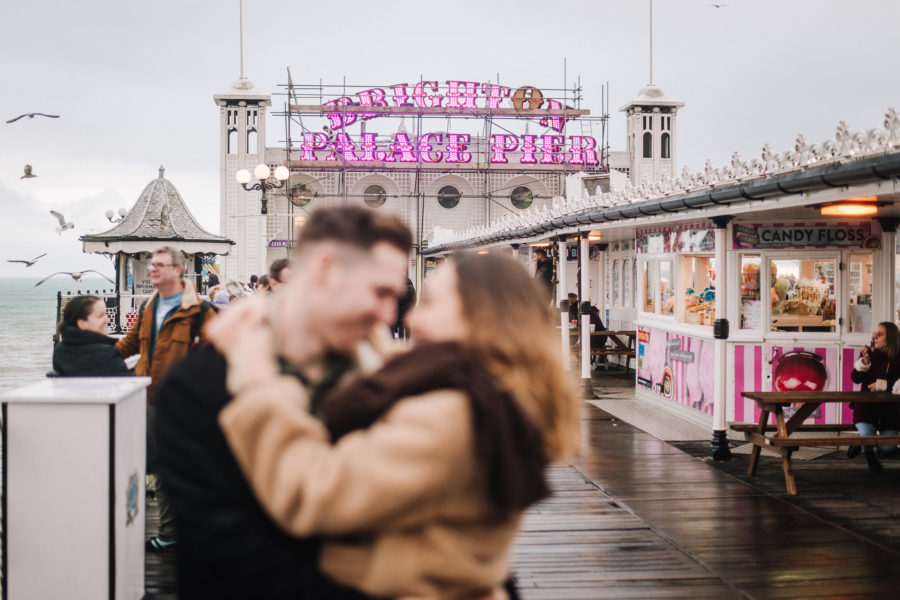 Coppia che si bacia sul Brighton Pier in mezzo alla gente, sotto alla pioggia