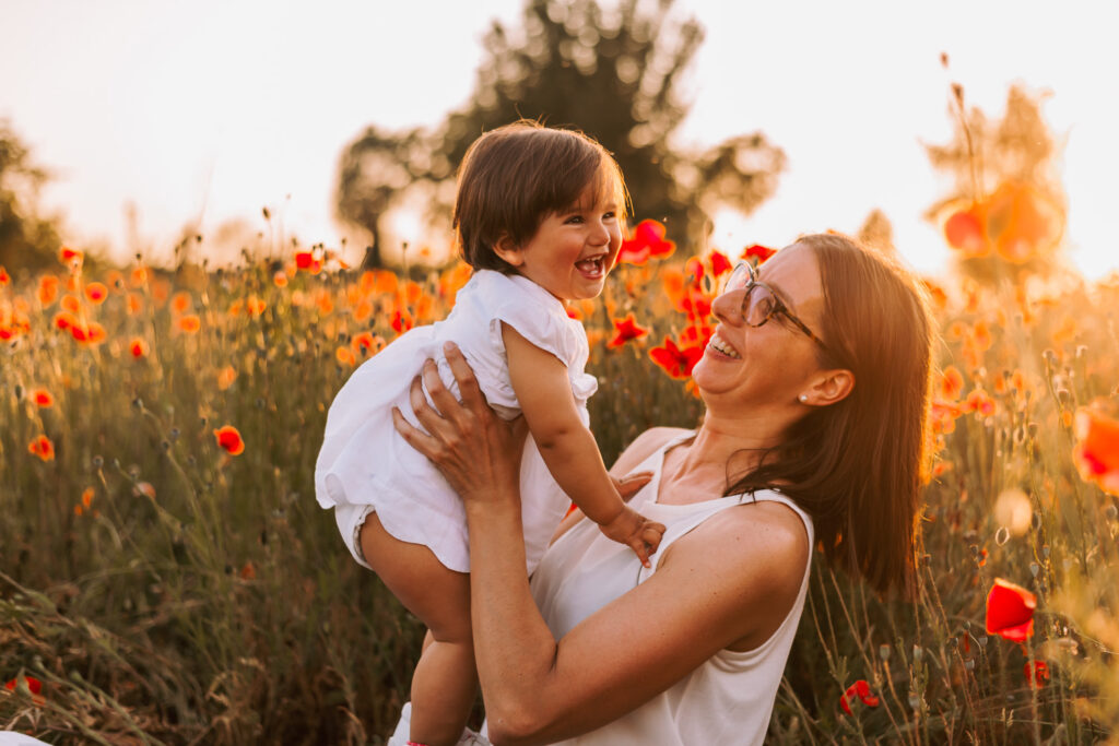 mamma che alza sua figlia tra i papaveri al tramonto